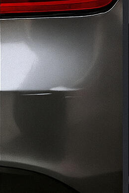 Close-up of a rear quarter panel dent on a silver vehicle, showcasing typical cosmetic damage covered in the guide